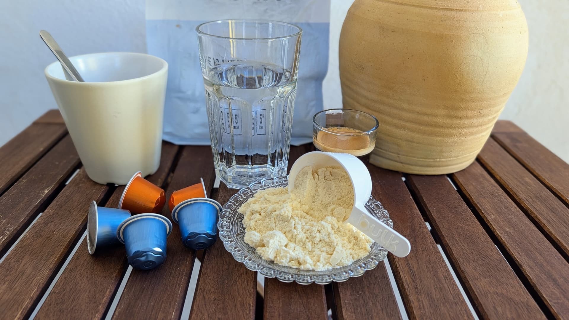 Polvo de colágeno hidrolizado con vaso de agua sobre mesa de madera exterior