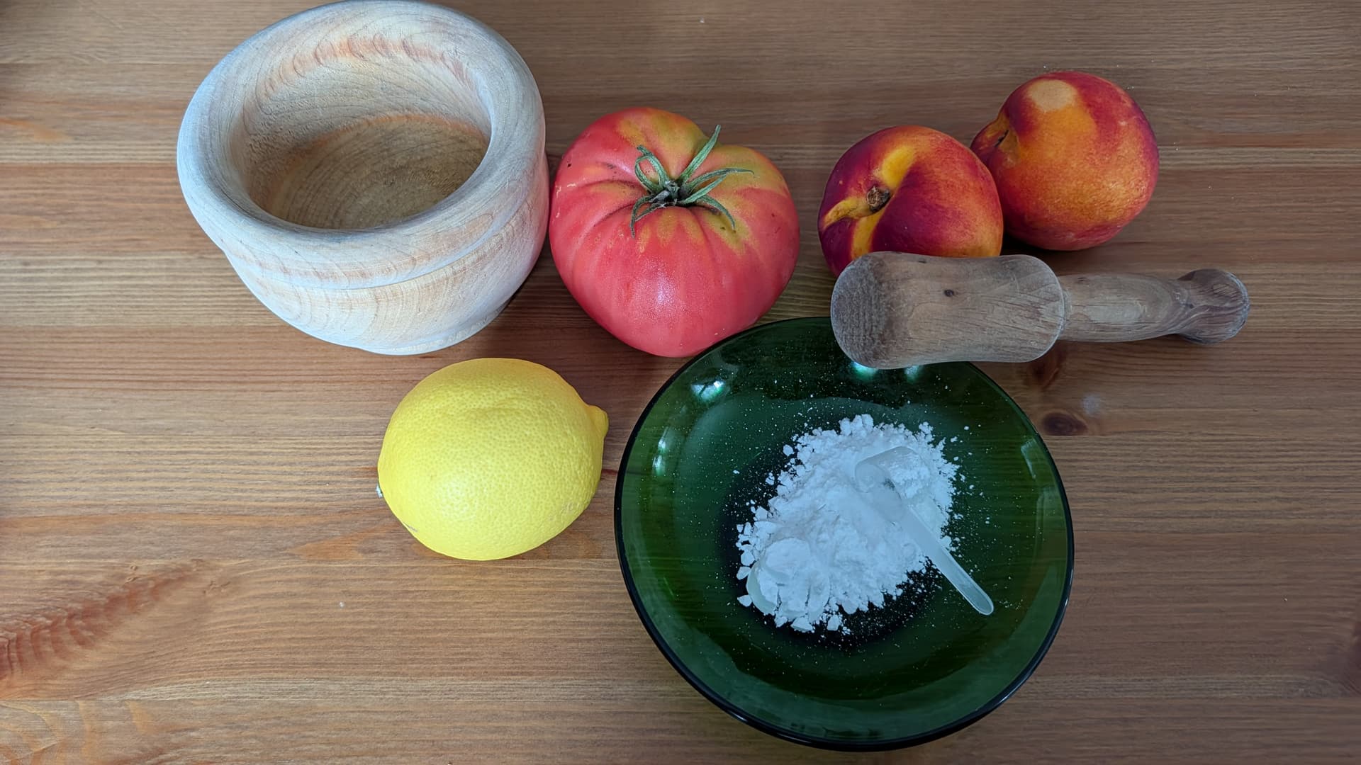 Plato de cristal verde tipo duralex con proteína en polvo junto con un limón, un tomate y dos nectarinas, además de un mortero de madera. Todo ello sobre mesa de madera.